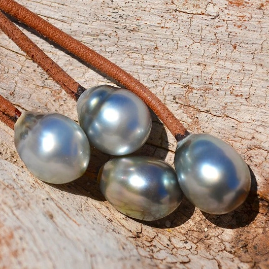 Close-up of the four Tahitian pearls and brown leather of the earrings on light wood