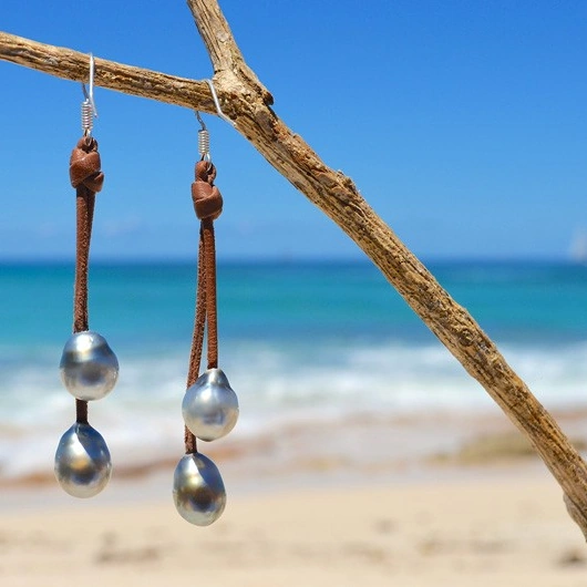 Brown leather drop earrings with four Tahitian pearls hanging from a branch by the sea
