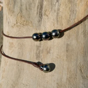 Leather choker with three 11.5 mm Tahitian pearls, on wood, detail.