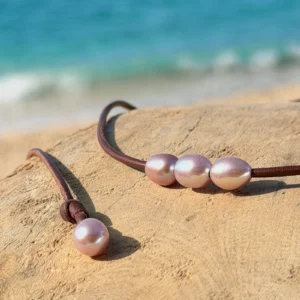 Leather choker with three oval pink pearls, on wood, detail.