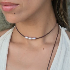 Leather choker with three oval pink pearls, worn around the neck.