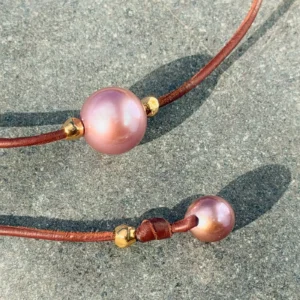 Ras du cou en cuir, perle rose et billes en plaqué or, sur une pierre, détail.