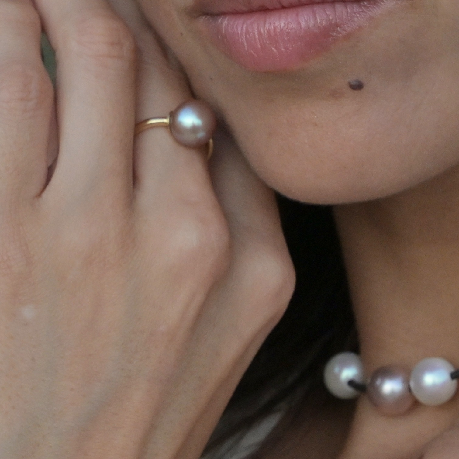 Precious gold ring with a pink pearl and diamond, close-up of the ring on the hand at the right of the photograph.