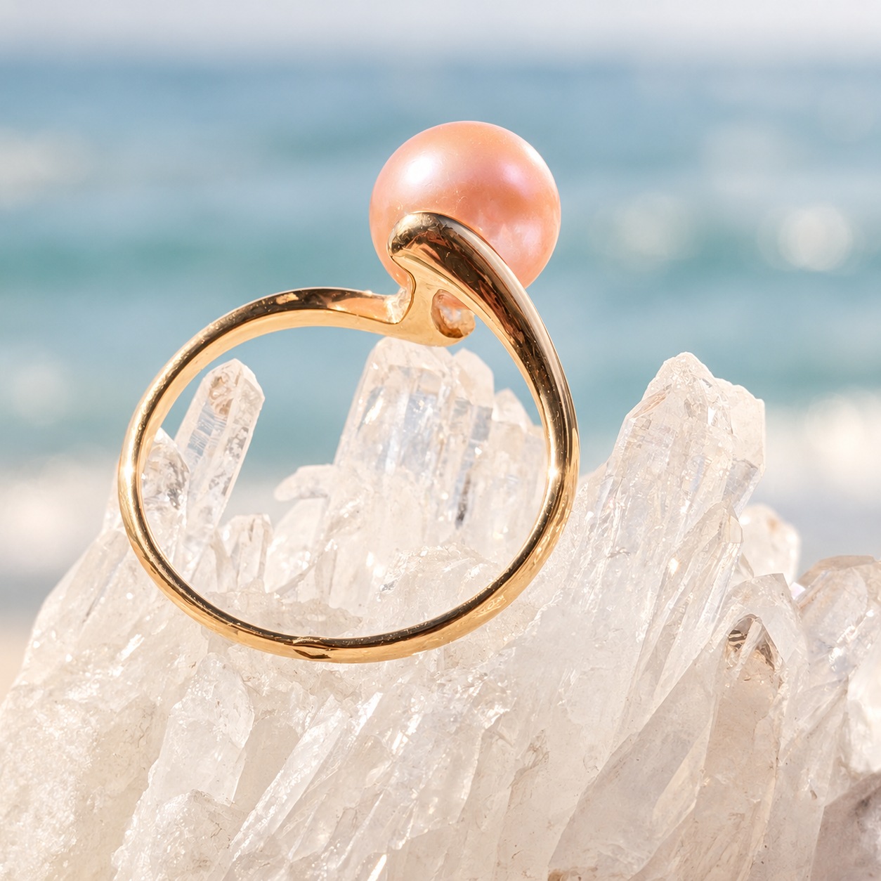 Wave ring in gold with a freshwater pearl, resting on crystals with the sea in the background.