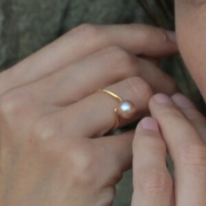 Bague Vague en or et perle d’eau douce, détail porté sur la main située à gauche de la photographie.