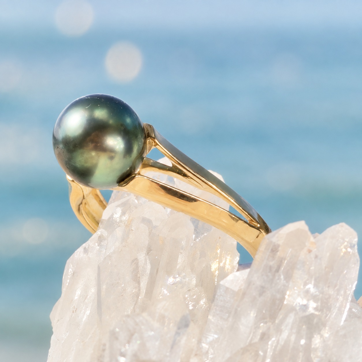 Bague Étreinte en or et perle verte de Tahiti, sur un support cristallin, vue de côté.
