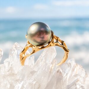 Bague en or 18 carats ajouré avec une perle de Tahiti, posée sur des cristaux devant la mer.
