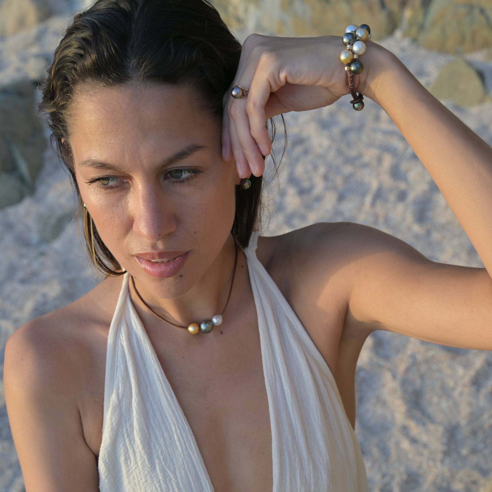 Bague Organique en or 18 carats et perle de Tahiti, vue portée contre un rocher, le bras levé.