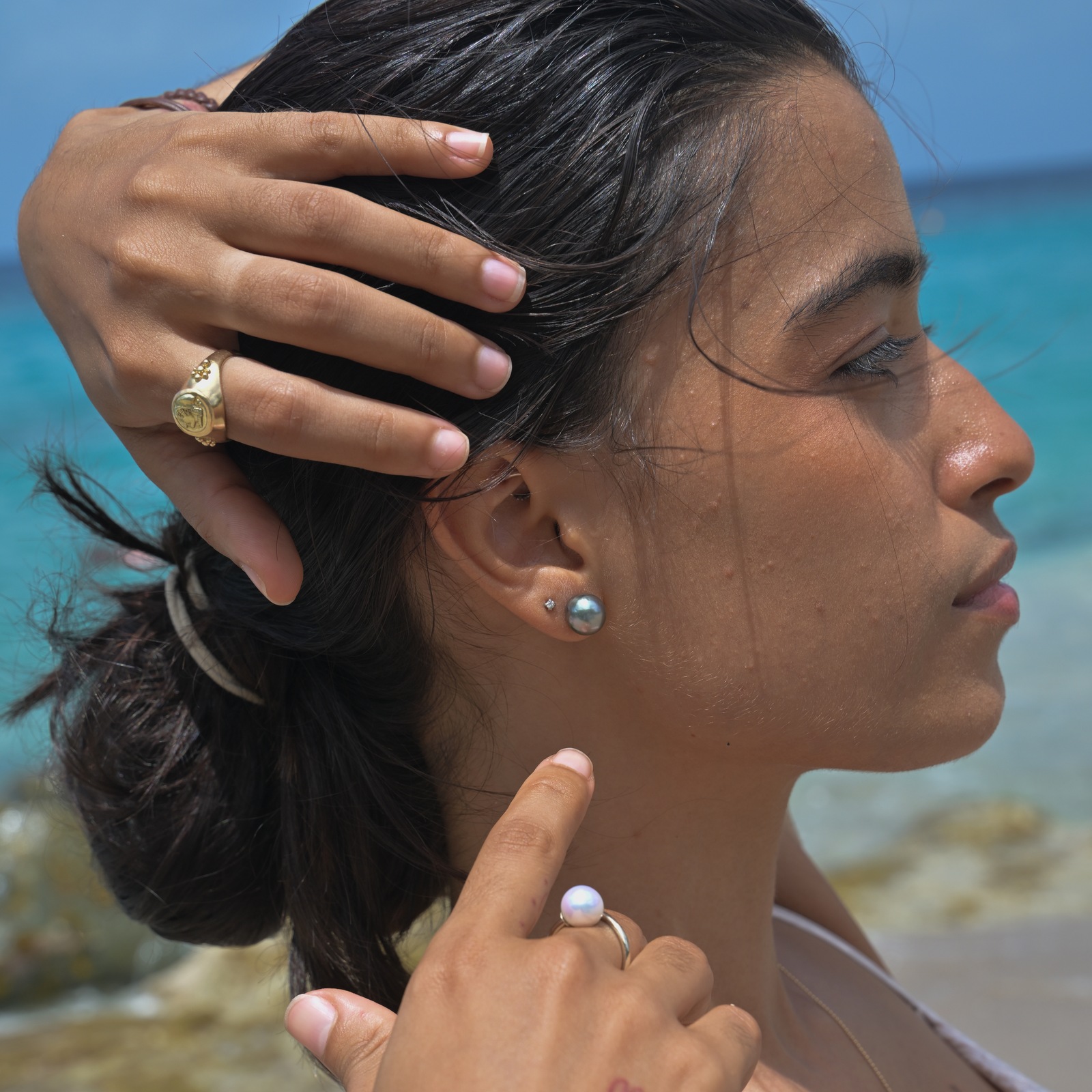 Clous en or 18 carats et perles de Tahiti, vue portée à l’oreille, portrait de profil avec la main dans les cheveux.