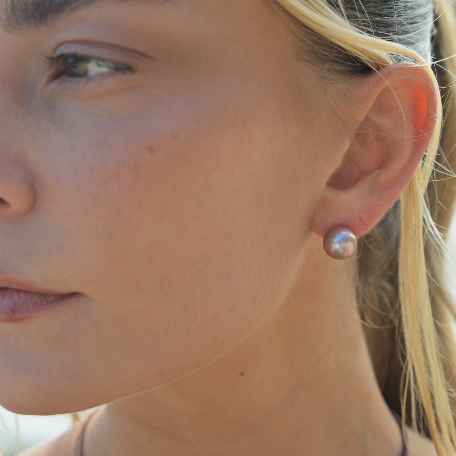 Clous en or 18 carats et perles roses d’eau douce, vue portée à l’oreille, portrait de profil en extérieur.