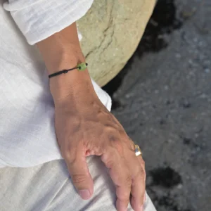 Bracelet ajustable en péridot brut sur cordon MOKUBA noir, porté au poignet.