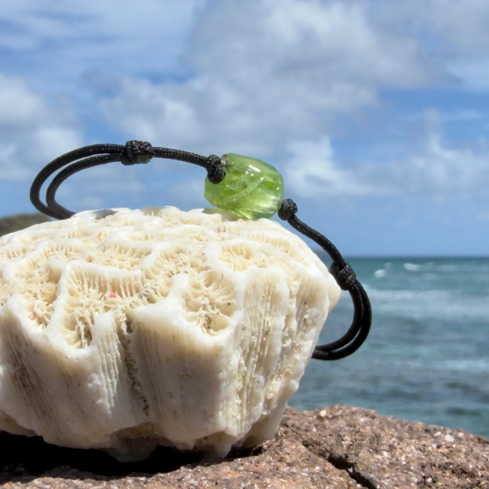 Bracelet en péridot brut sur cordon MOKUBA noir sans billes métalliques, photographié devant la mer.
