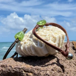 Bracelet double cuir et péridot, fermoir perle, sur un support de corail, plusieurs modèles visibles.