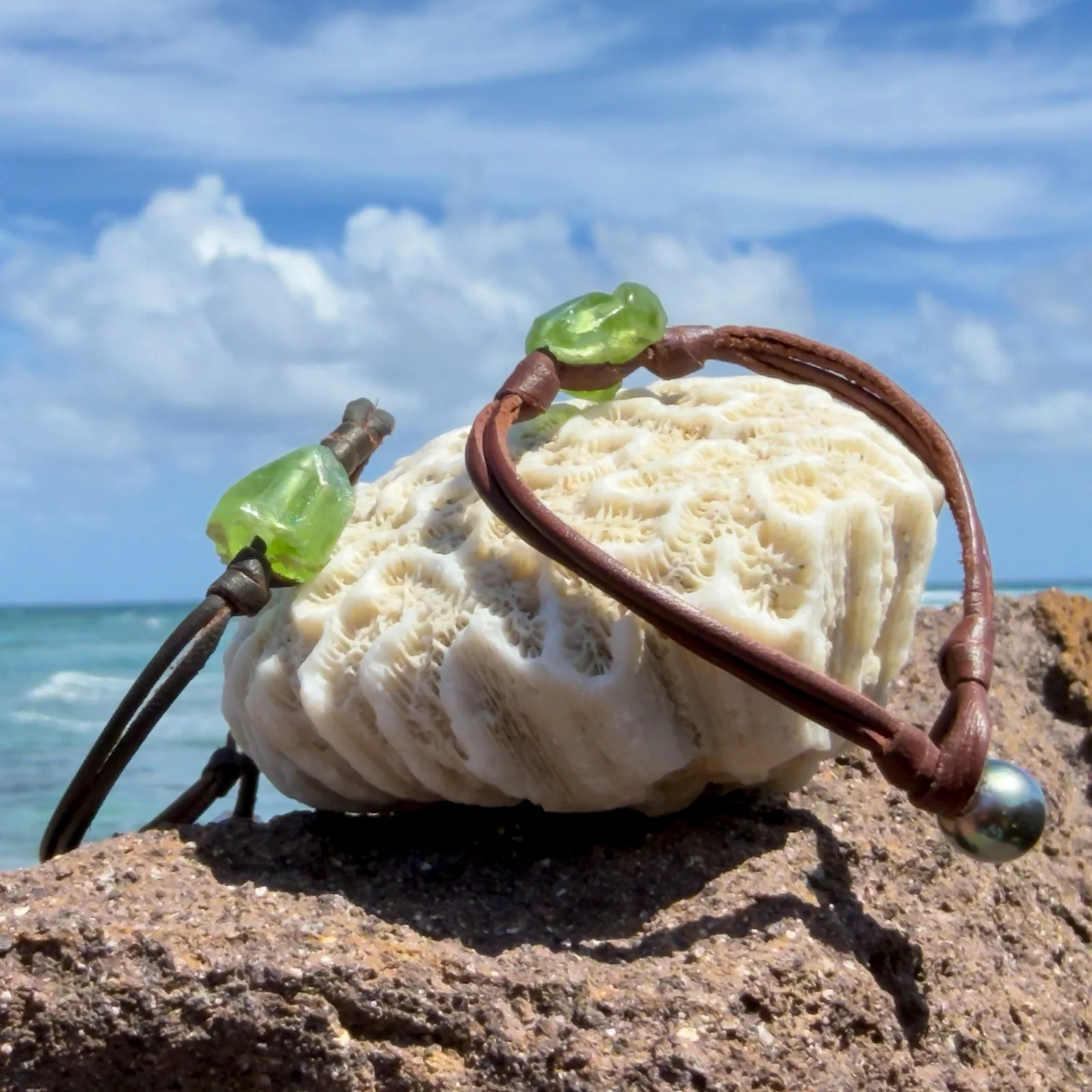 Bracelet double cuir et péridot, fermoir perle, sur un support de corail, plusieurs modèles visibles.