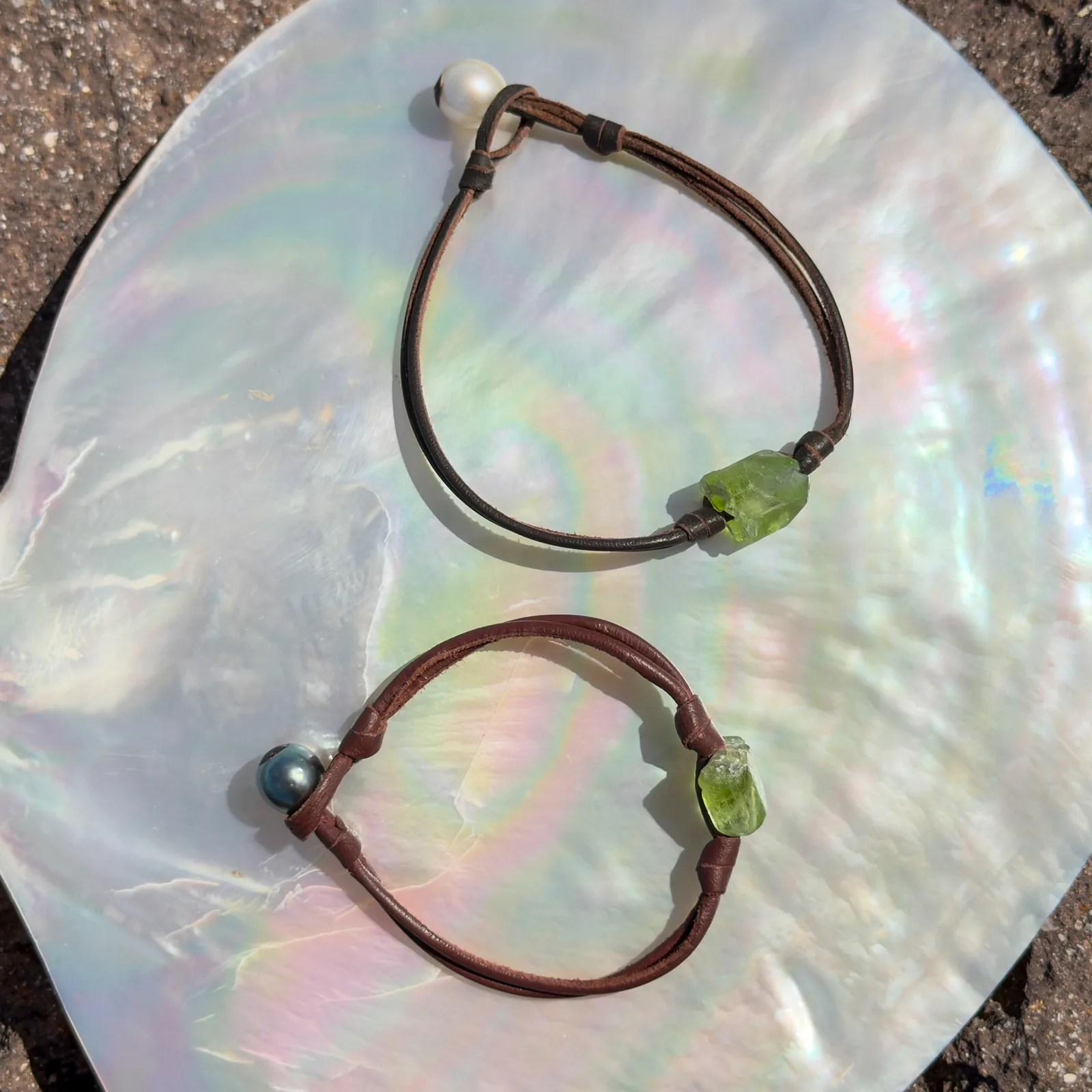 Bracelet double cuir et péridot, fermoir perle, sur un coquillage, plusieurs modèles visibles.