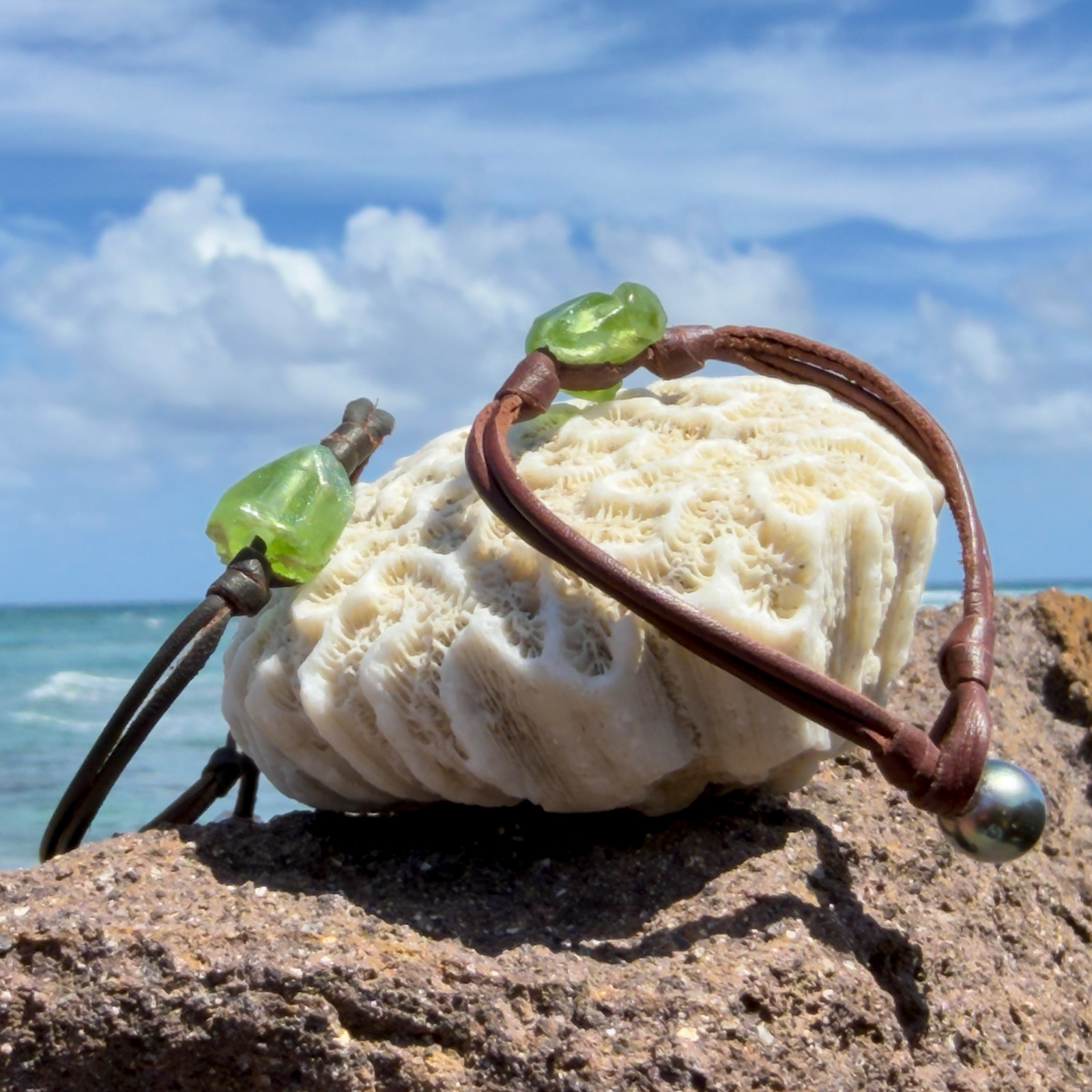 Bracelet double cuir et péridot, fermoir perle, sur un support de corail, plusieurs modèles visibles.