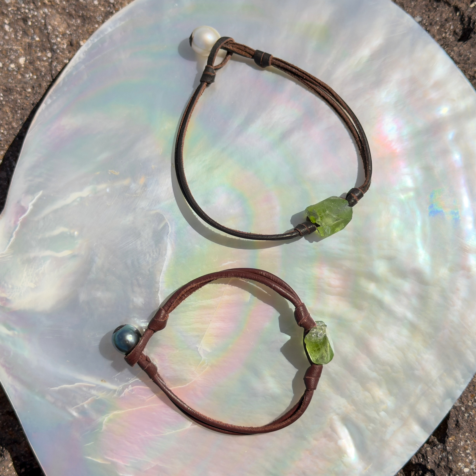 Bracelet double cuir et péridot, fermoir perle, sur un coquillage, plusieurs modèles visibles.