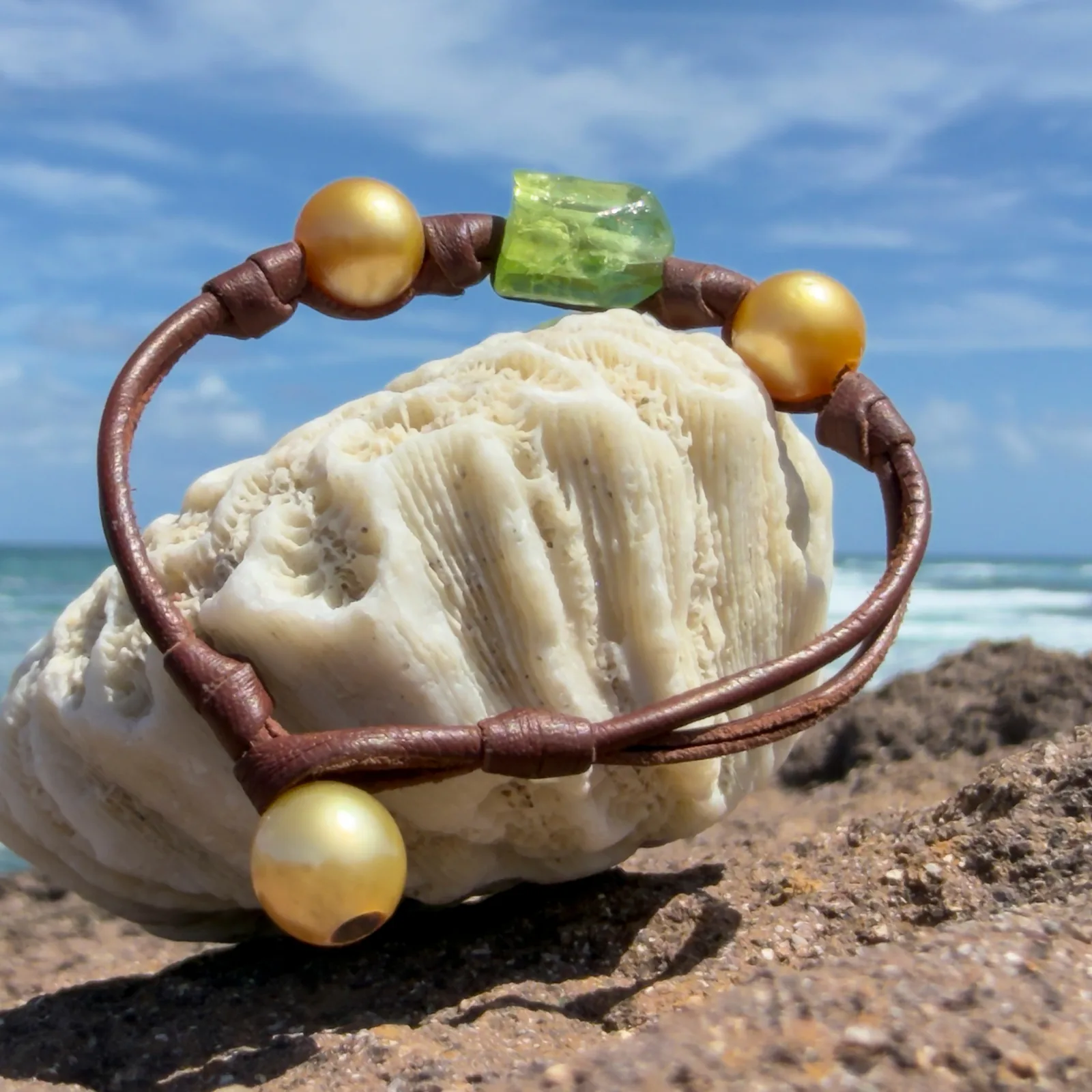 Bracelet en cuir, péridot et deux perles, perles dorées, sur un support de corail.