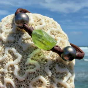 Bracelet en cuir, péridot et deux perles, perles foncées, sur un support de corail.