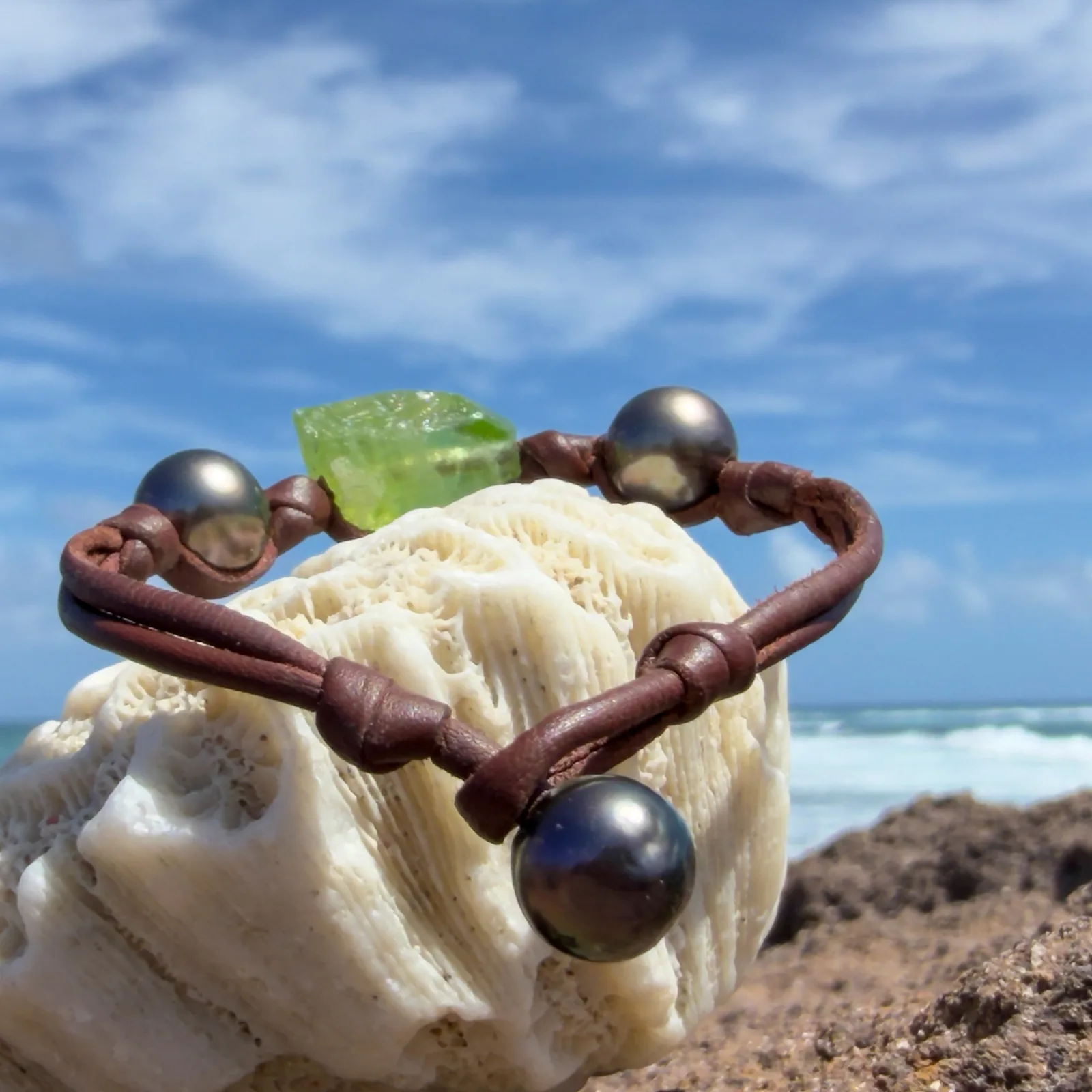 Bracelet en cuir, péridot et deux perles, fermoir en perle foncée, sur un support de corail, vue arrière.