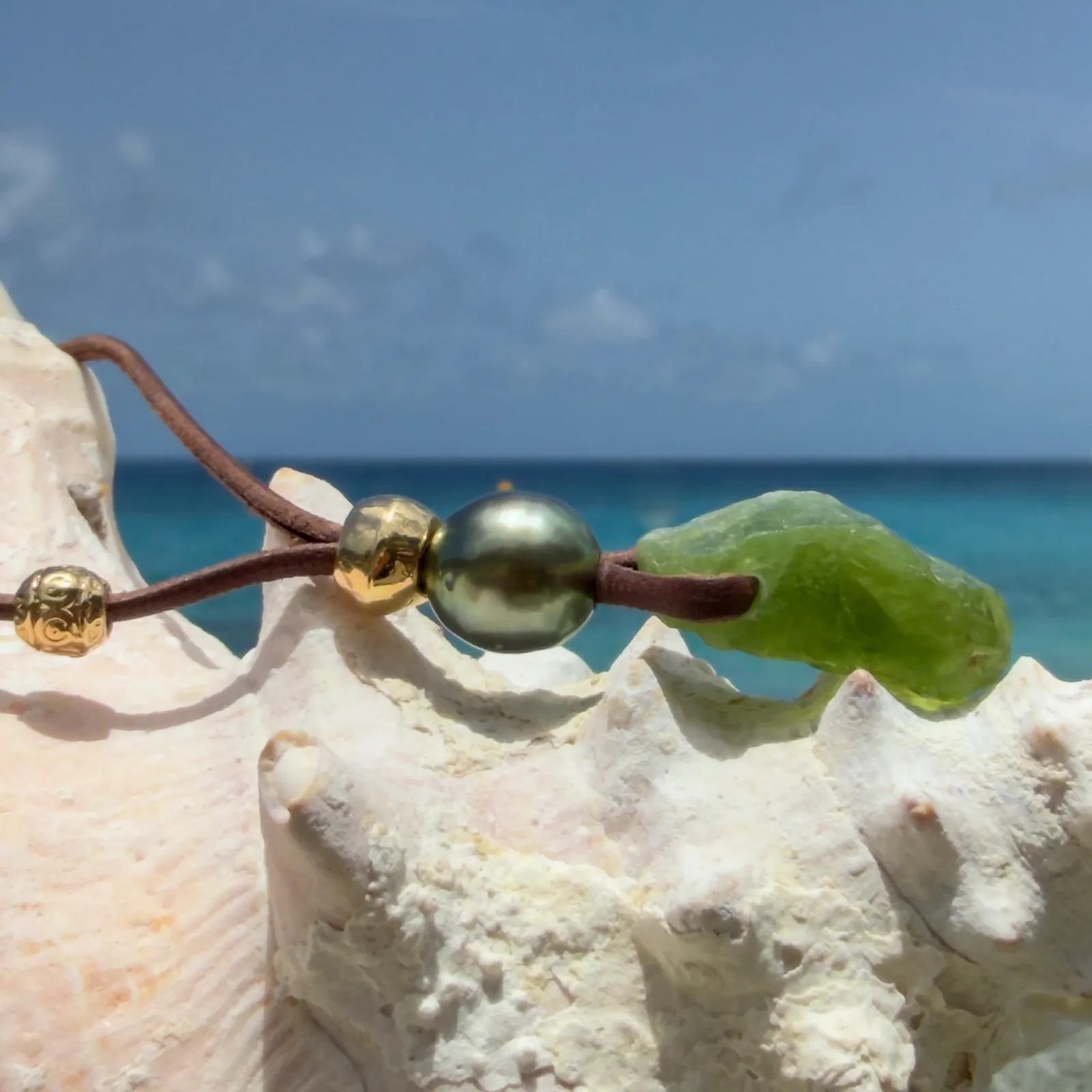 Leather necklace with a peridot pendant and a pearl, dark pearl, on a shell.