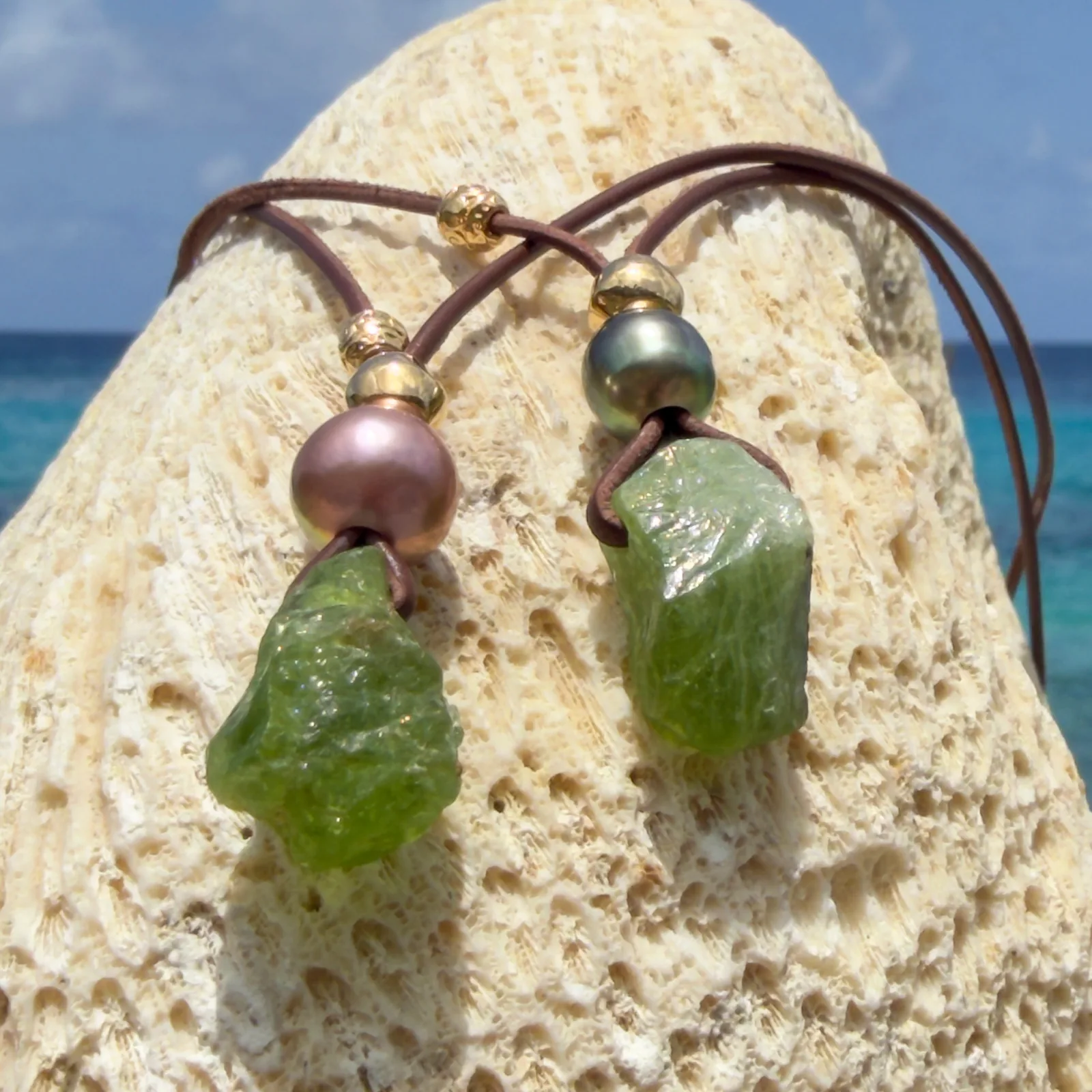 Leather necklace with a peridot pendant and a pearl, two variants shown together, on wood.