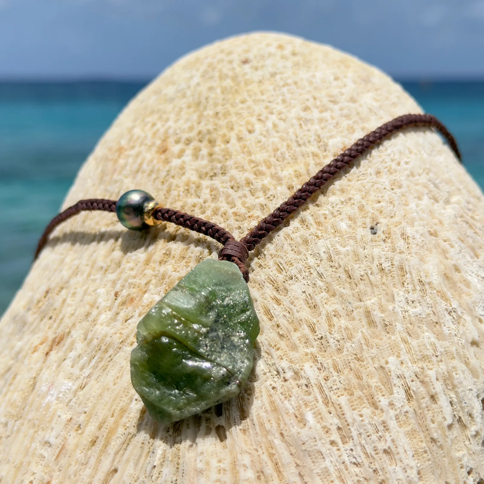 Braided leather necklace with a peridot pendant, on wood.