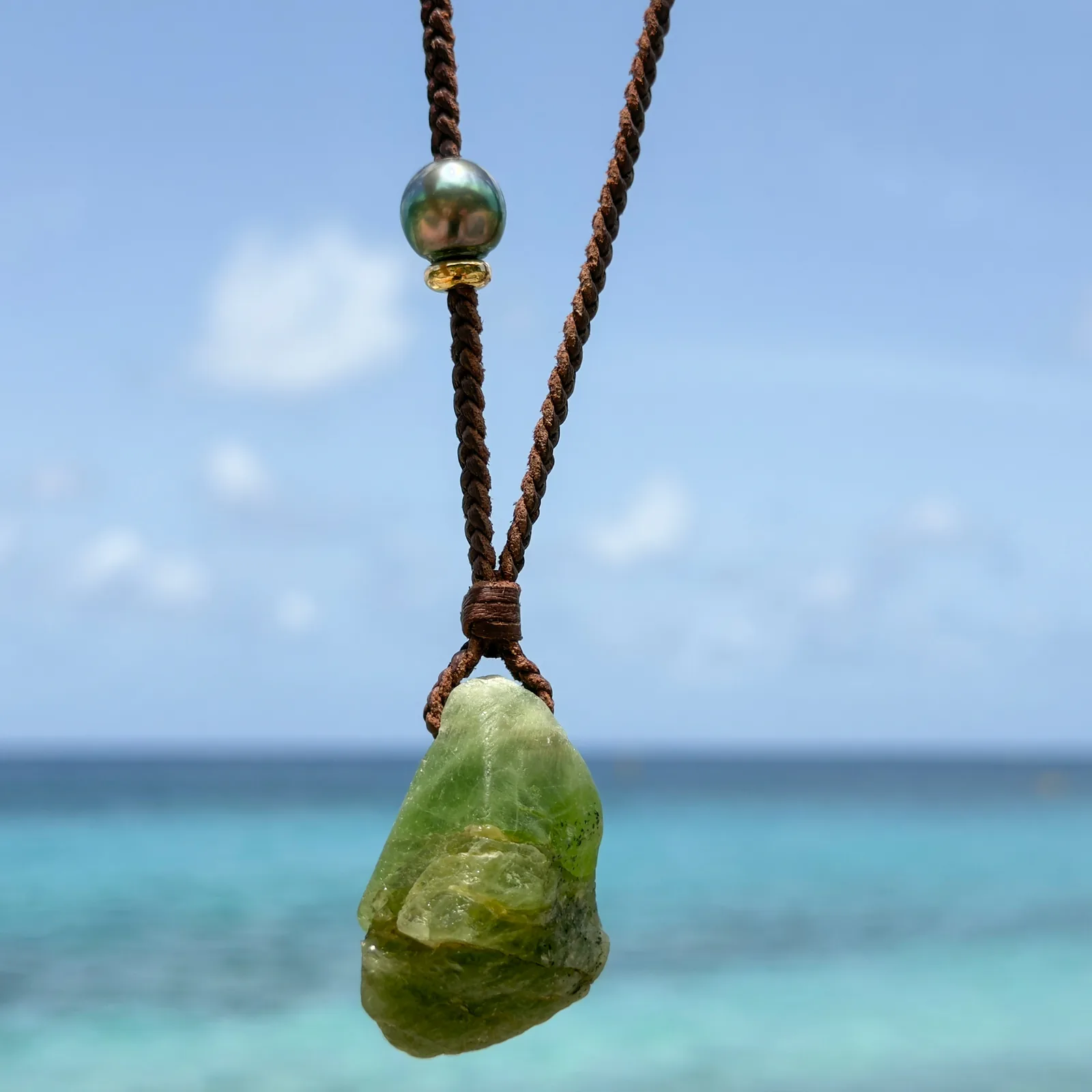 Braided leather necklace with a peridot pendant, hanging freely.