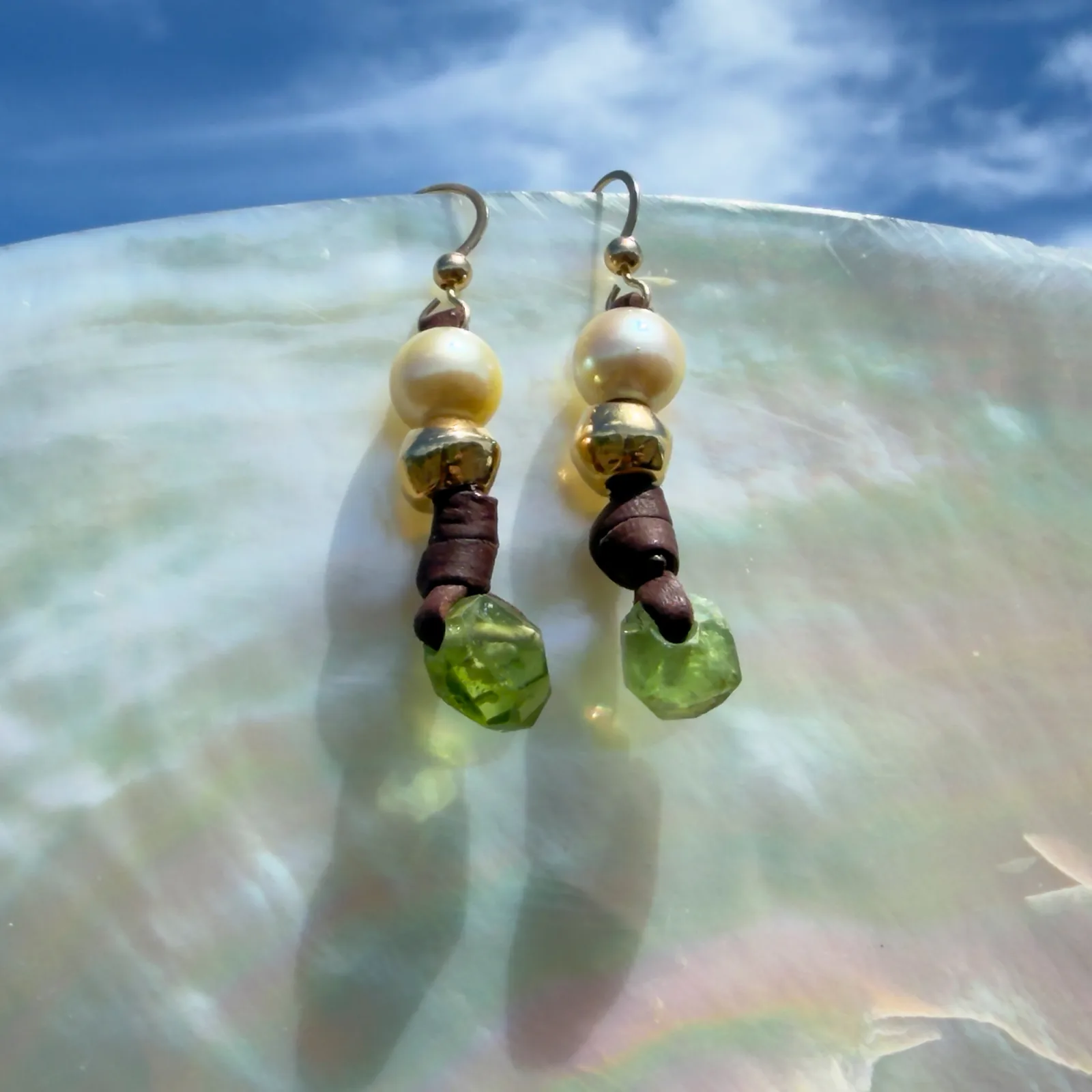 Boucles d’oreilles en cuir, perles des mers du Sud et péridot, sur un coquillage.