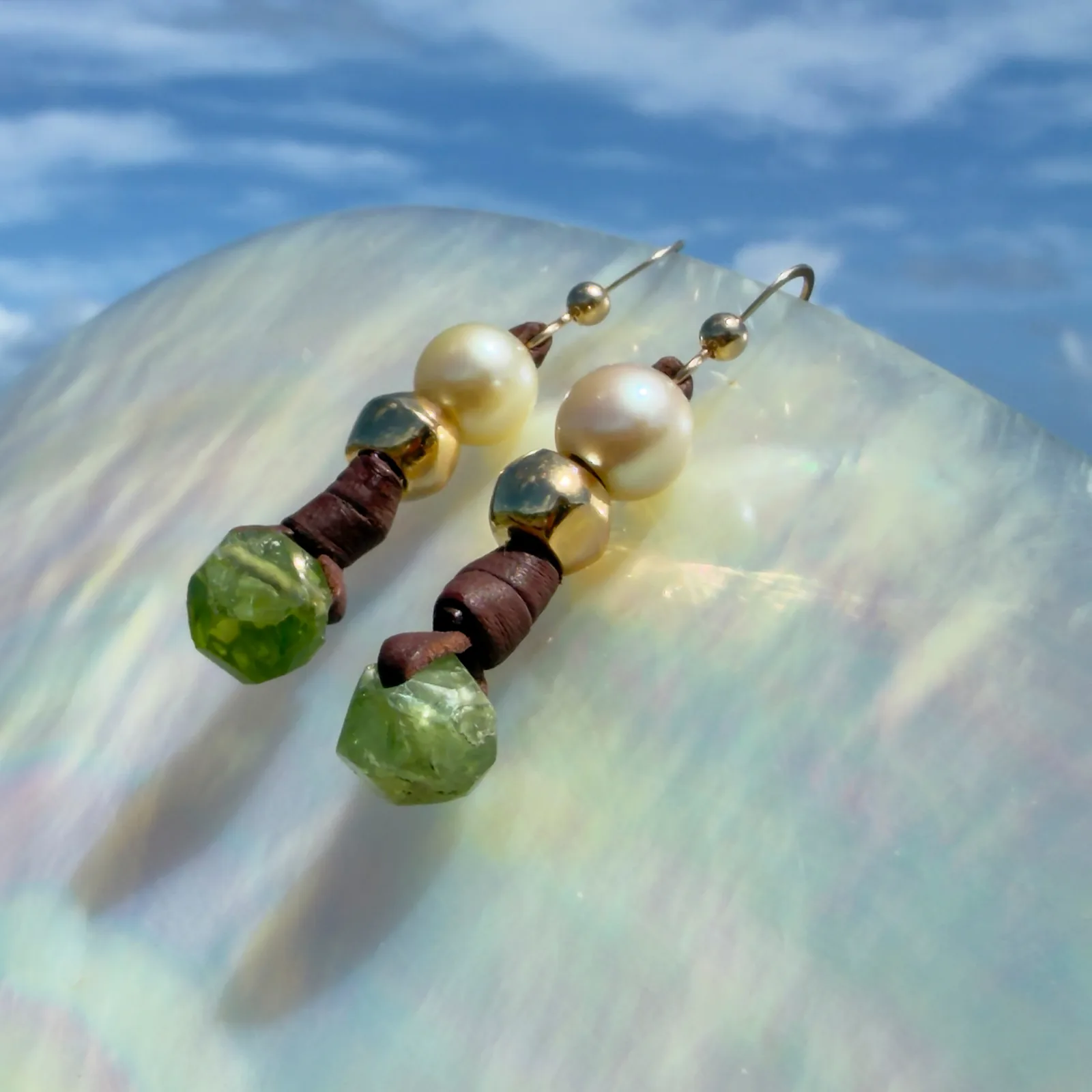 Boucles d’oreilles en cuir, perles des mers du Sud et péridot, sur un coquillage, vue de côté.