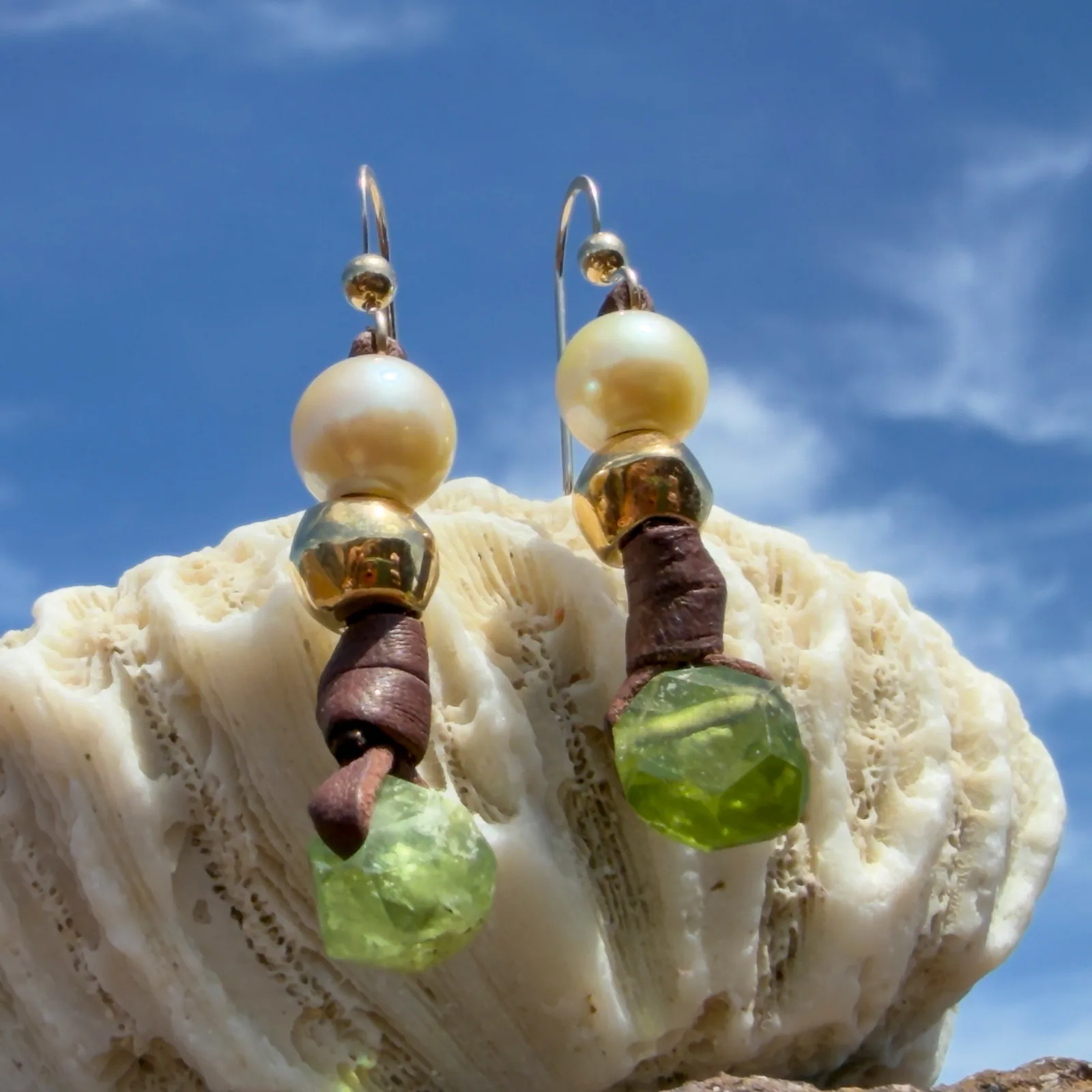 Boucles d’oreilles en cuir, perles des mers du Sud et péridot, sur un support de corail, vue de côté.