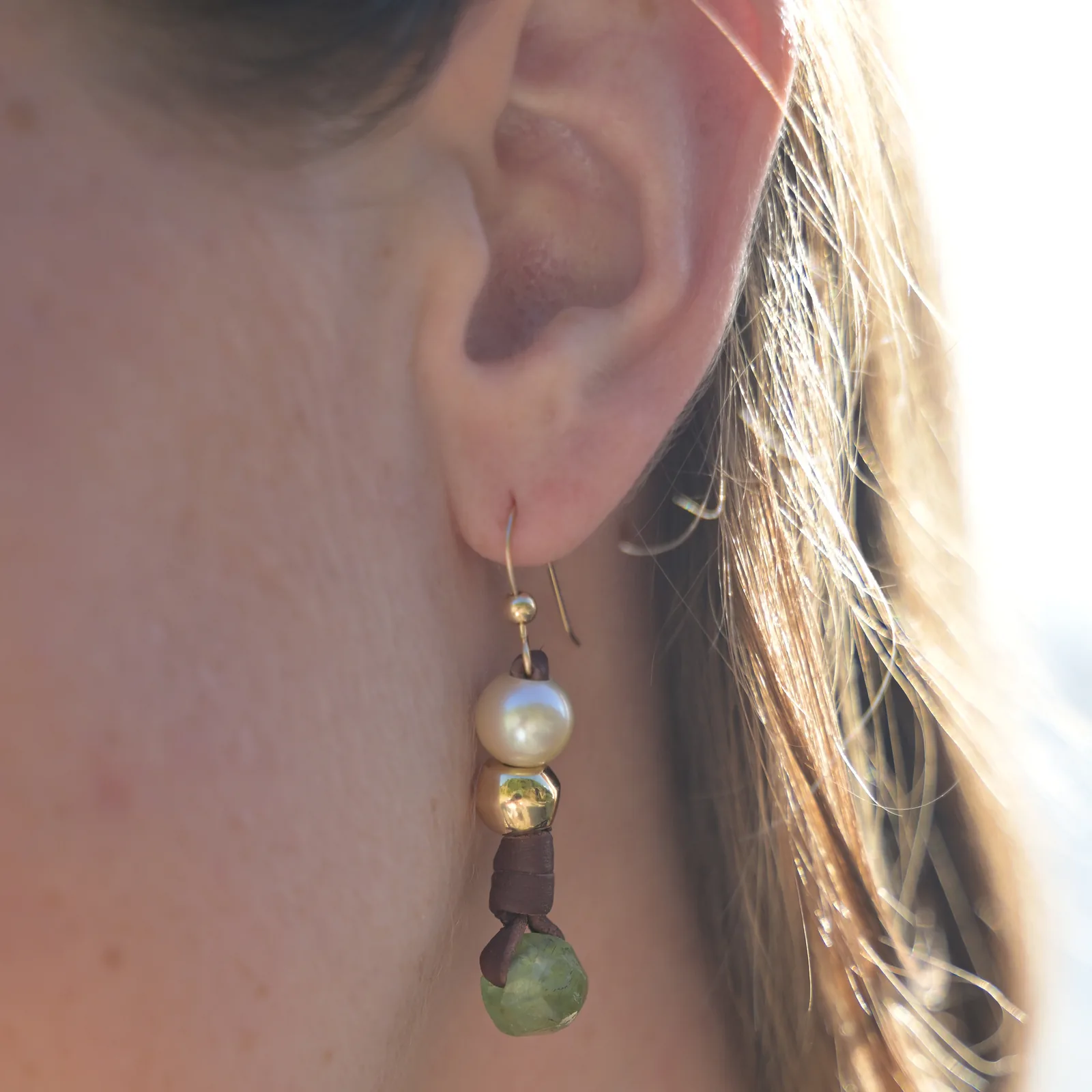 Boucles en cuir, perles des mers du Sud et péridot, portées de profil.