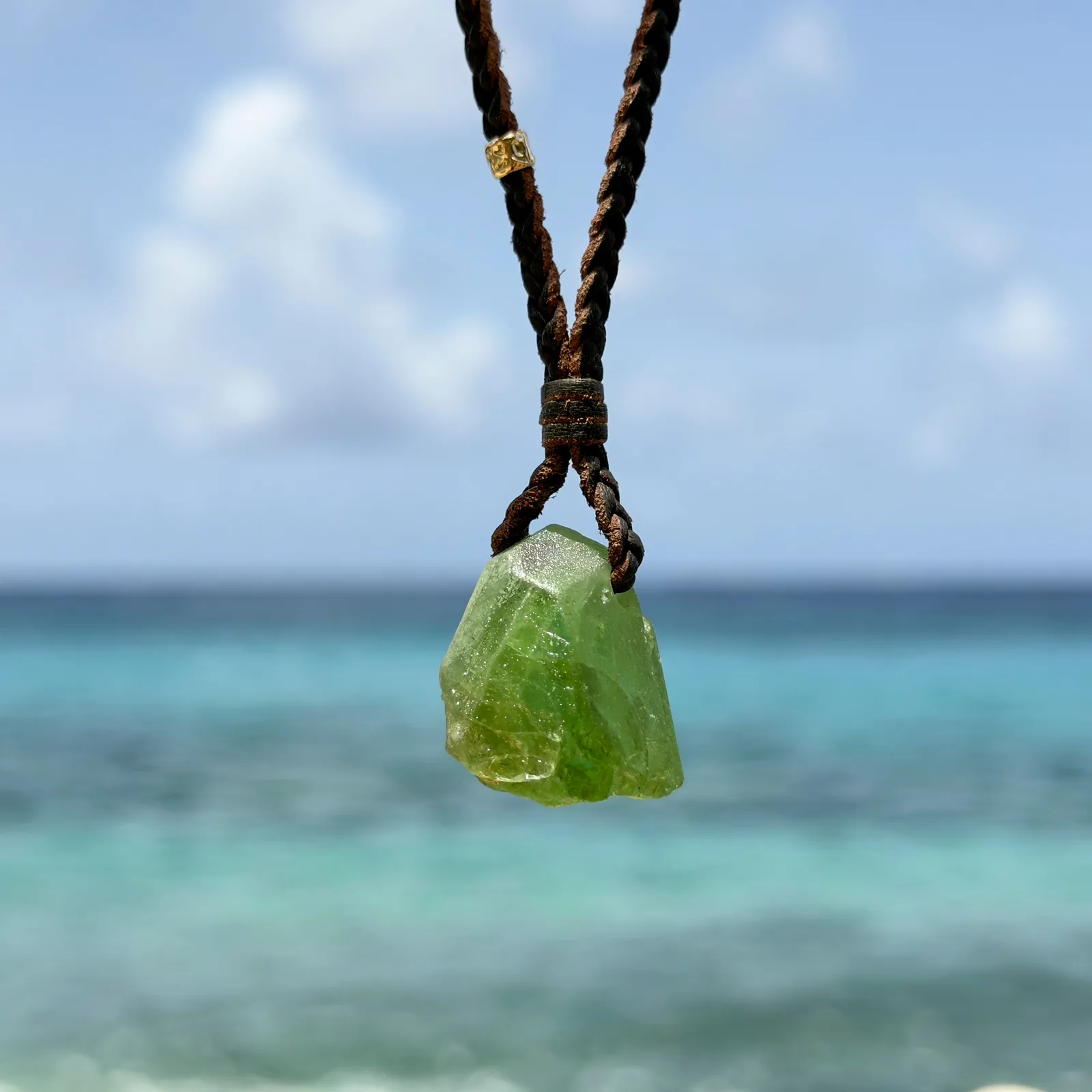 Braided leather necklace with a peridot pendant, hanging freely.