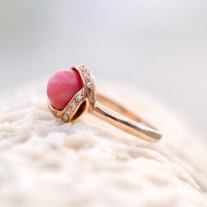 Bague en or rose, perle de lambis et diamants, posée sur du corail, vue de côté.