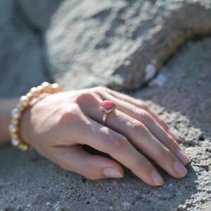 Bague en or rose, perle de lambis et diamants, portée sur une main posée sur un rocher.