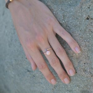 Bague Toi et Moi en or, perle de lambis et saphir, portée sur une main posée sur un rocher.