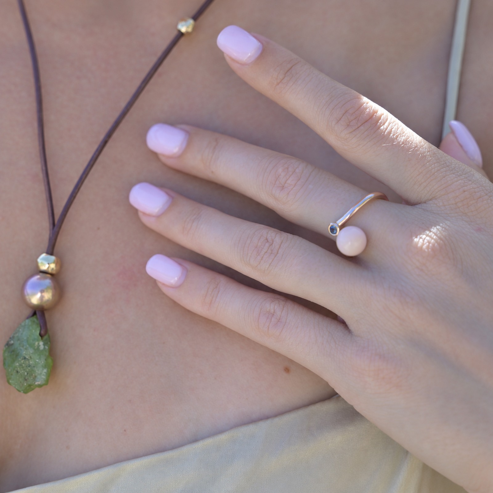 Bague Toi et Moi en or, perle de lambis et saphir, portée sur la main, avec des colliers visibles au décolleté.