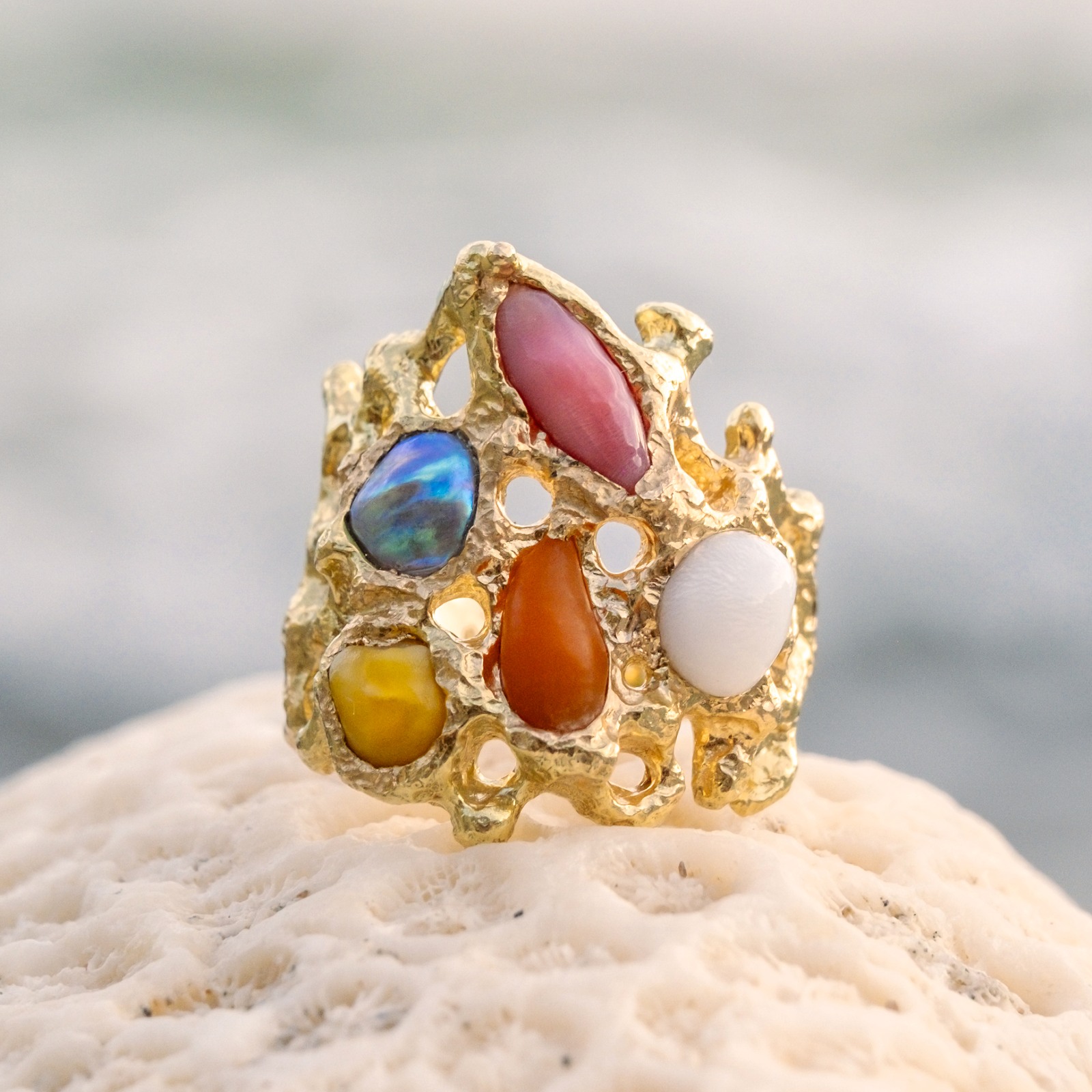 Bague Corail en or et perles fines multicolores, posée sur du corail, vue de face.