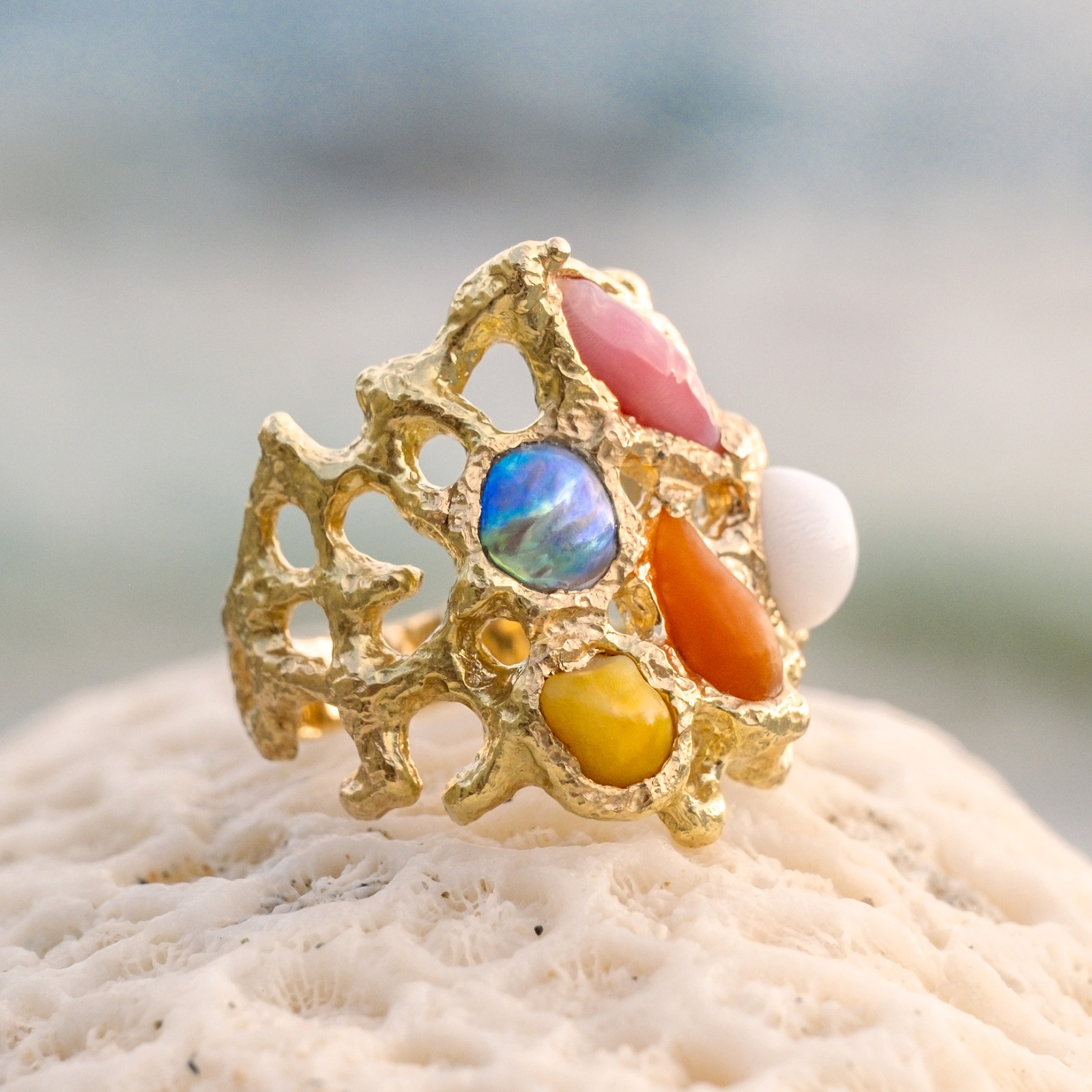 Bague Corail en or et perles fines multicolores, posée sur du corail, vue de trois quarts.