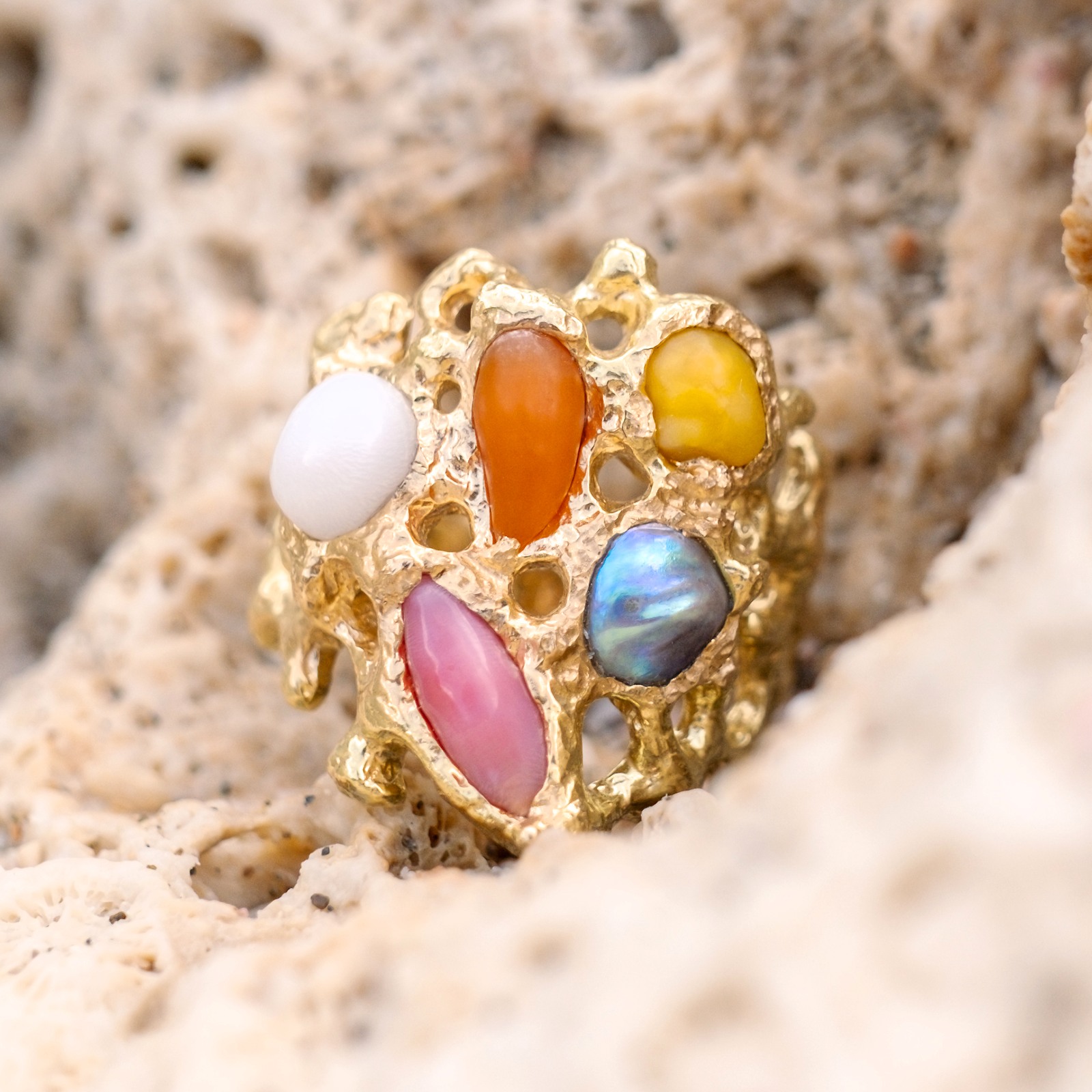 Bague Corail en or et perles fines multicolores, gros plan des perles et de la monture posée sur du corail.