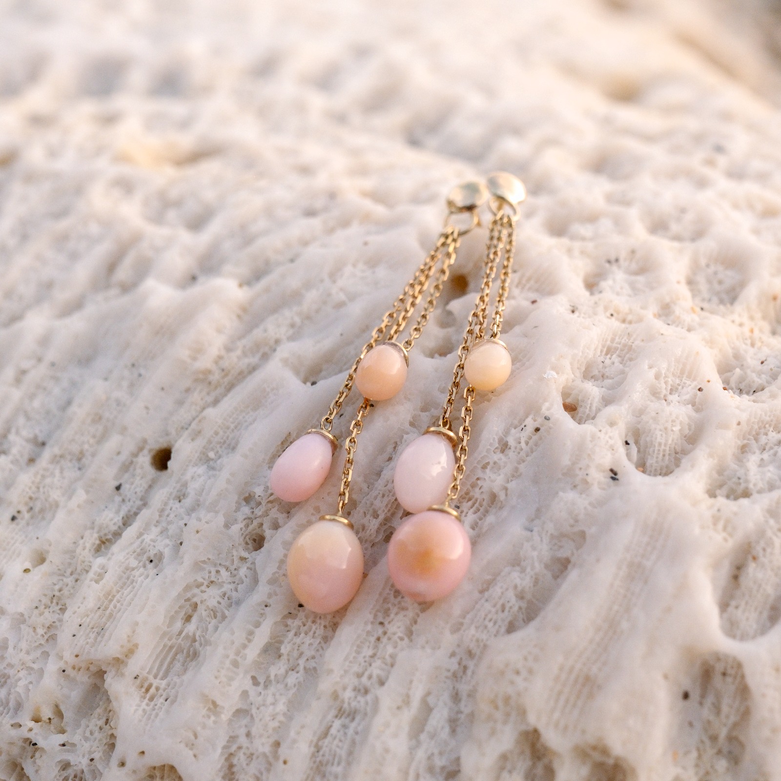 Boucles pendantes en or et 6 perles de lambis, paire posée sur du corail, vue d’ensemble.