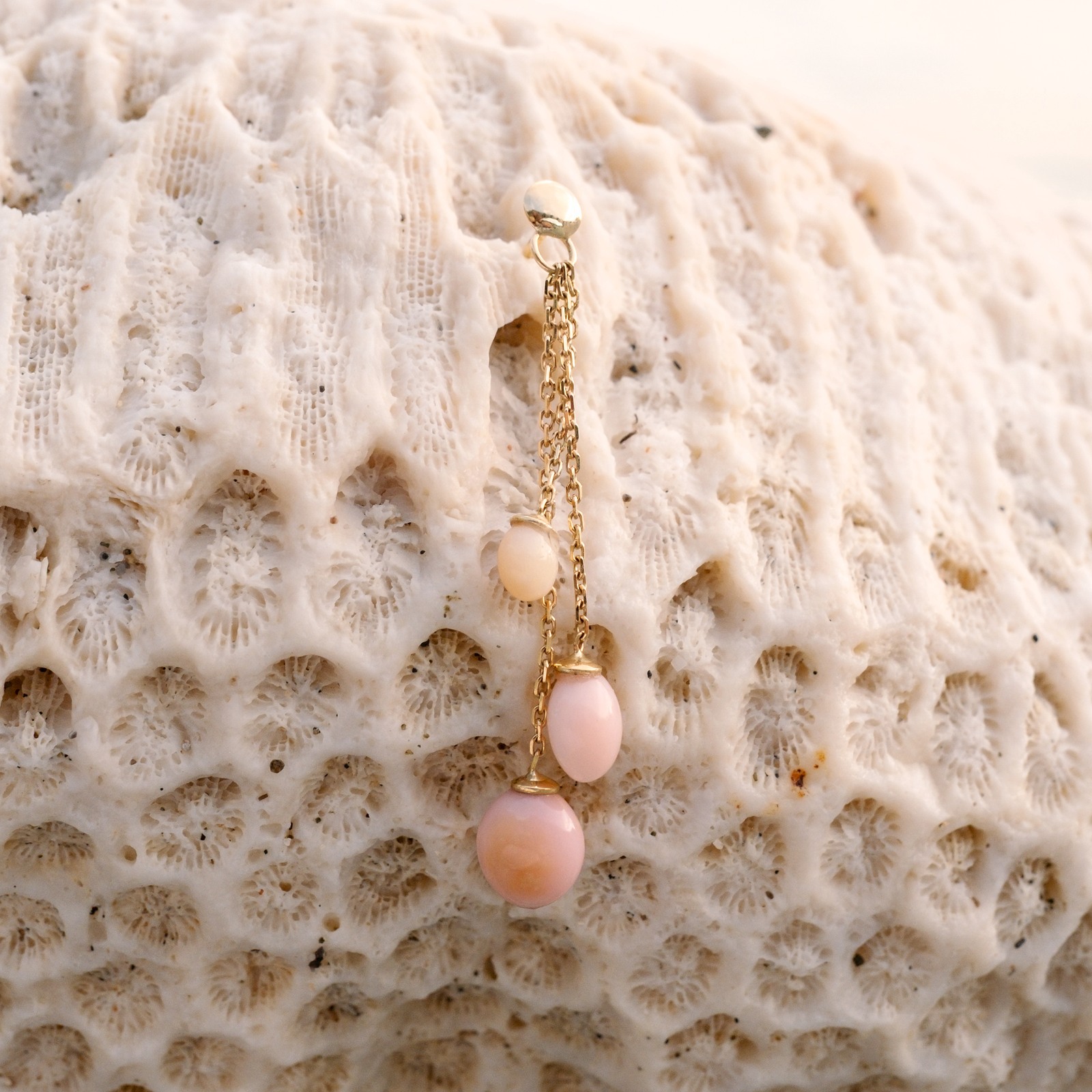 Boucle pendante en or et perles de lambis, une boucle posée sur du corail, détail de ses 3 perles.