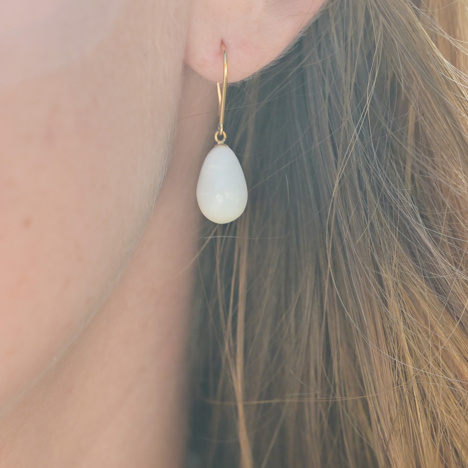 Boucles en or et perles fines de bénitier en gouttes, gros plan d’une boucle portée à l’oreille.