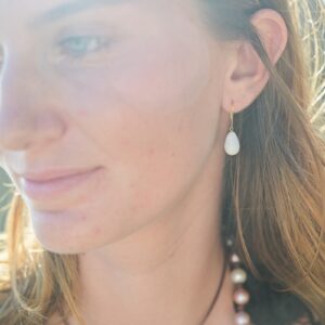Boucles en or et perles fines de bénitier en gouttes, une boucle portée, vue rapprochée du visage en lumière naturelle.