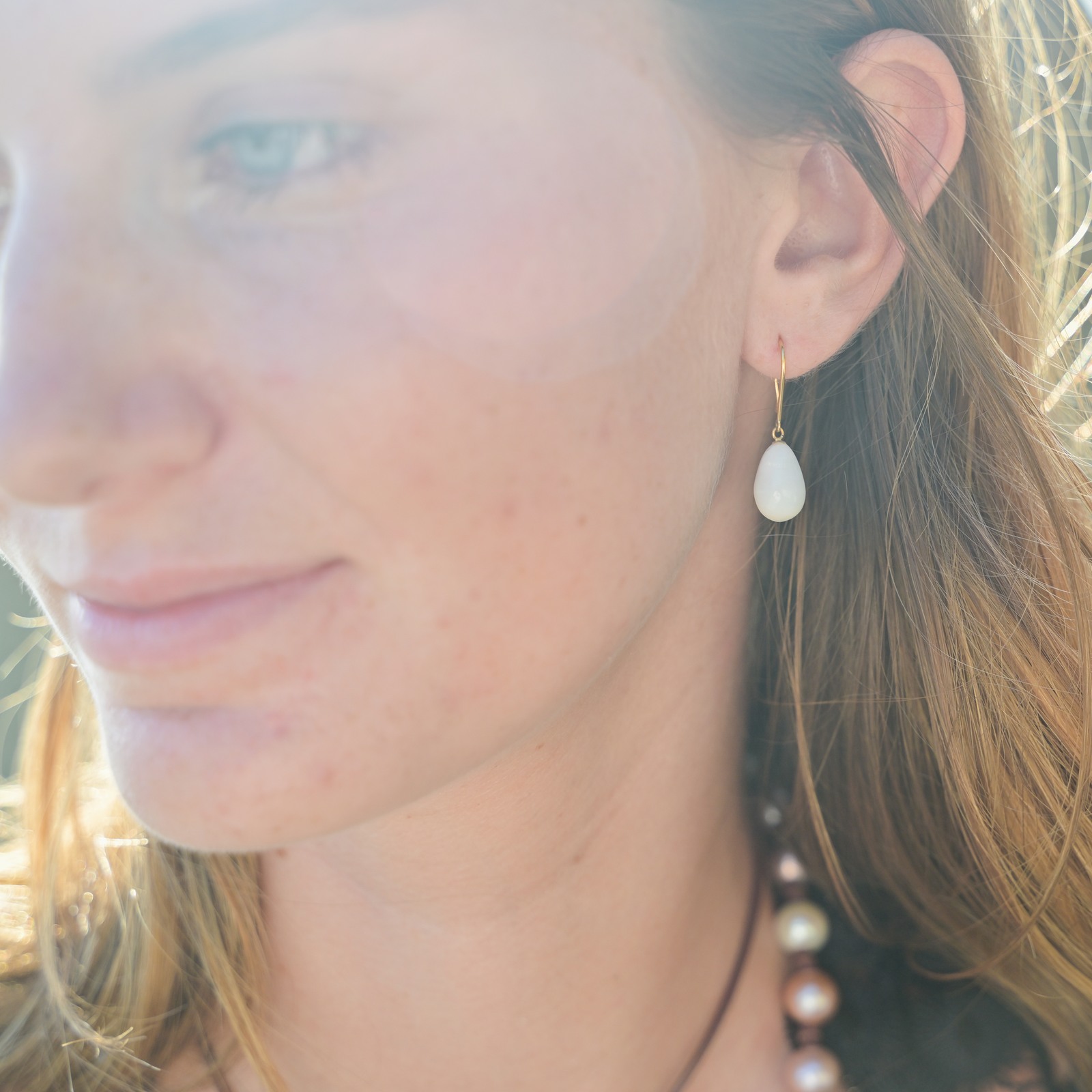 Boucles en or et perles fines de bénitier en gouttes, une boucle portée, vue rapprochée du visage en lumière naturelle.