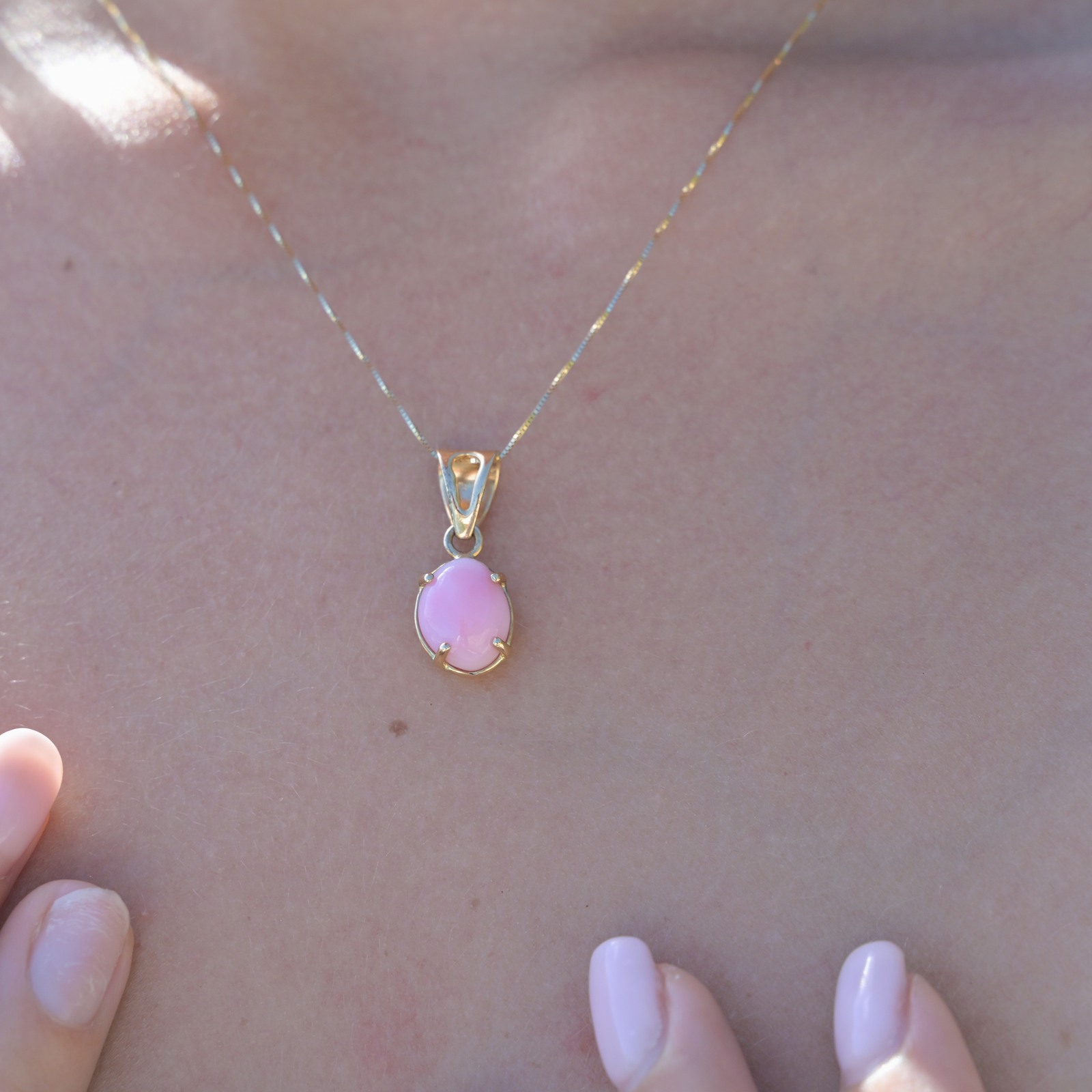 Gold pendant with a pink conch pearl, close-up of the pendant worn at the neckline.