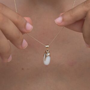 Gold pendant with an elongated natural clam pearl, close-up of the pendant held between the hands.