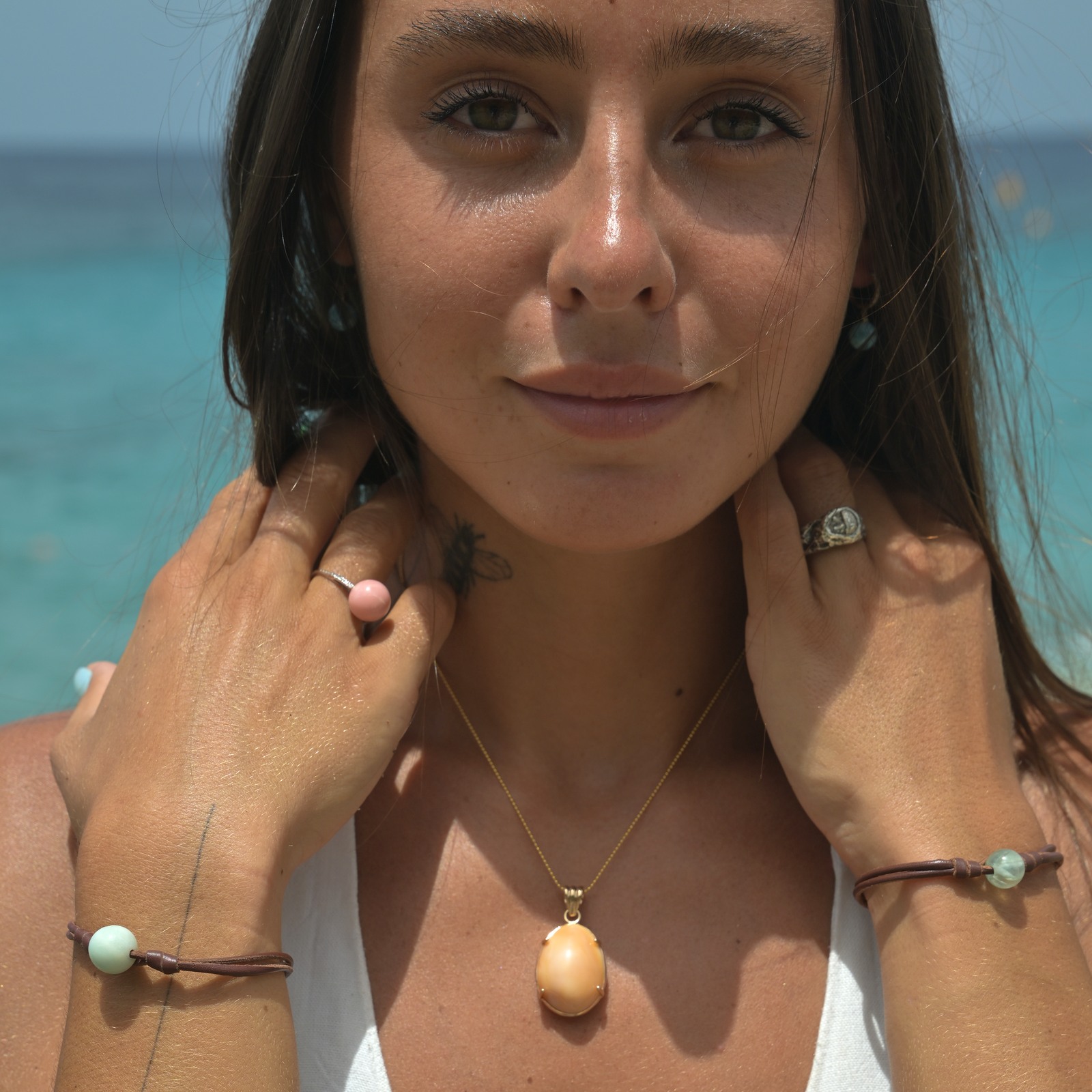 Gold pendant with a natural cassis cornuta pearl, worn in a front-facing portrait with the model’s face and hands.