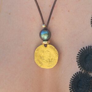 Leather pendant necklace with a gold escudo and a Tahitian pearl, close-up on the model.