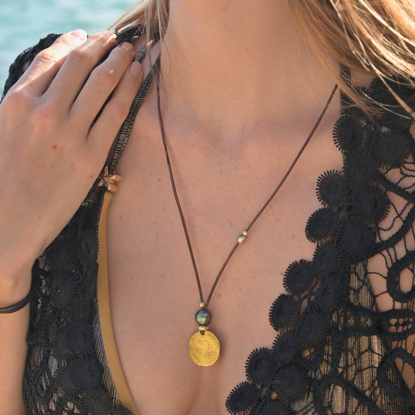 Leather pendant necklace with a gold escudo and a Tahitian pearl, close-up showing the visible necklace without the model’s face.